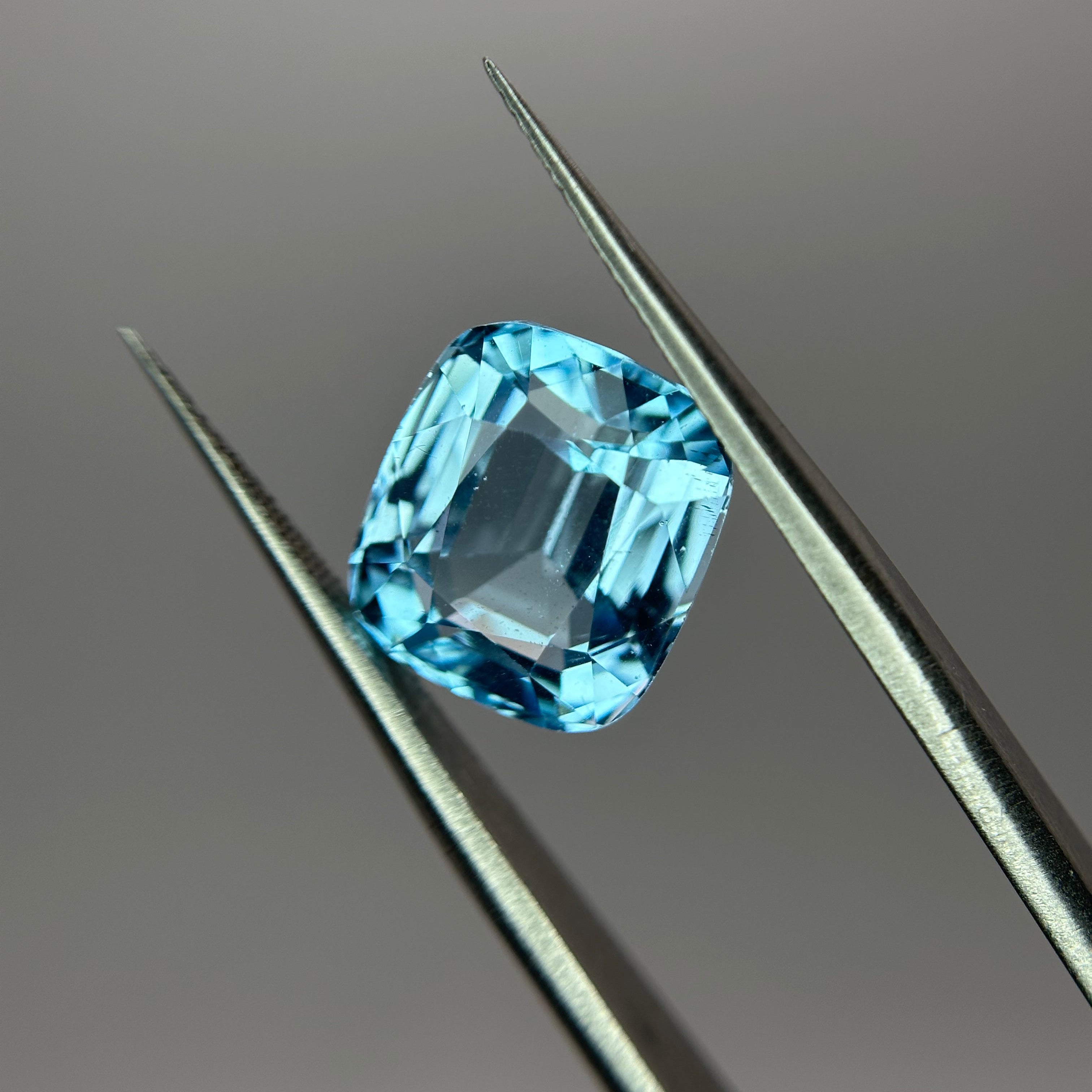Blue gemstone held by tweezers on a gray background