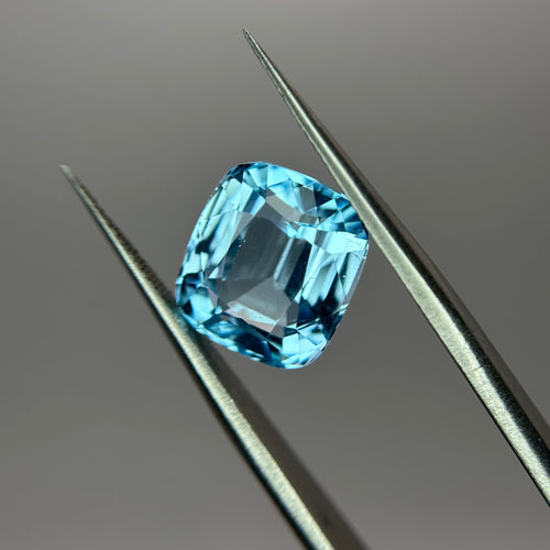 Blue gemstone held by tweezers on a gray background
