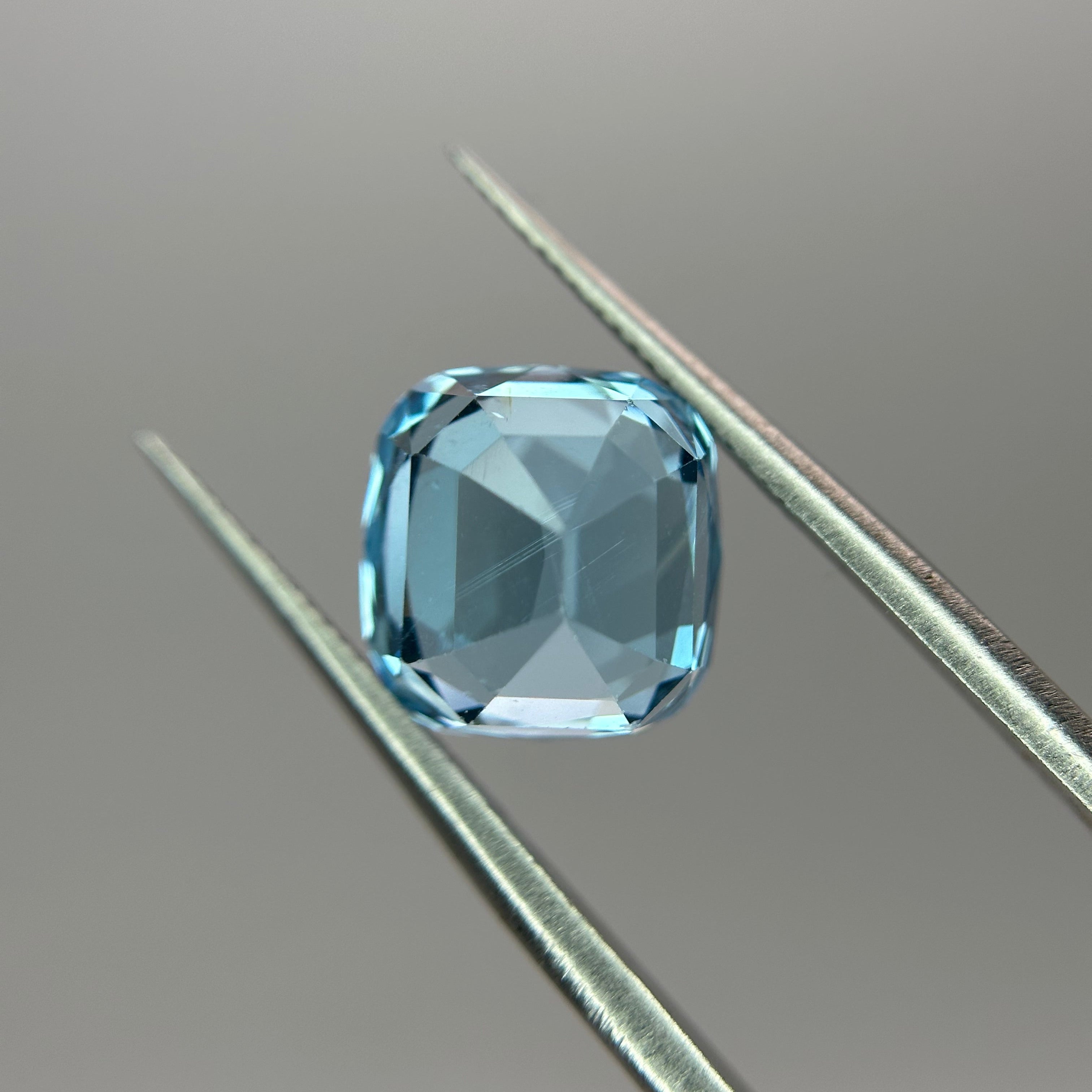 Blue gemstone held between tweezers on a gray background